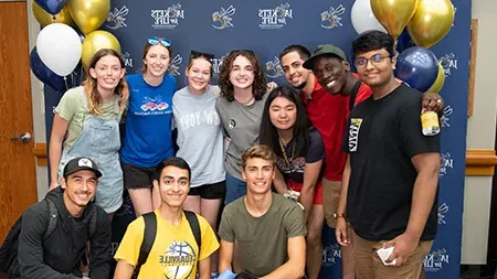 Group of eleven students smiling in front of Jackets for Life photo backdrop.